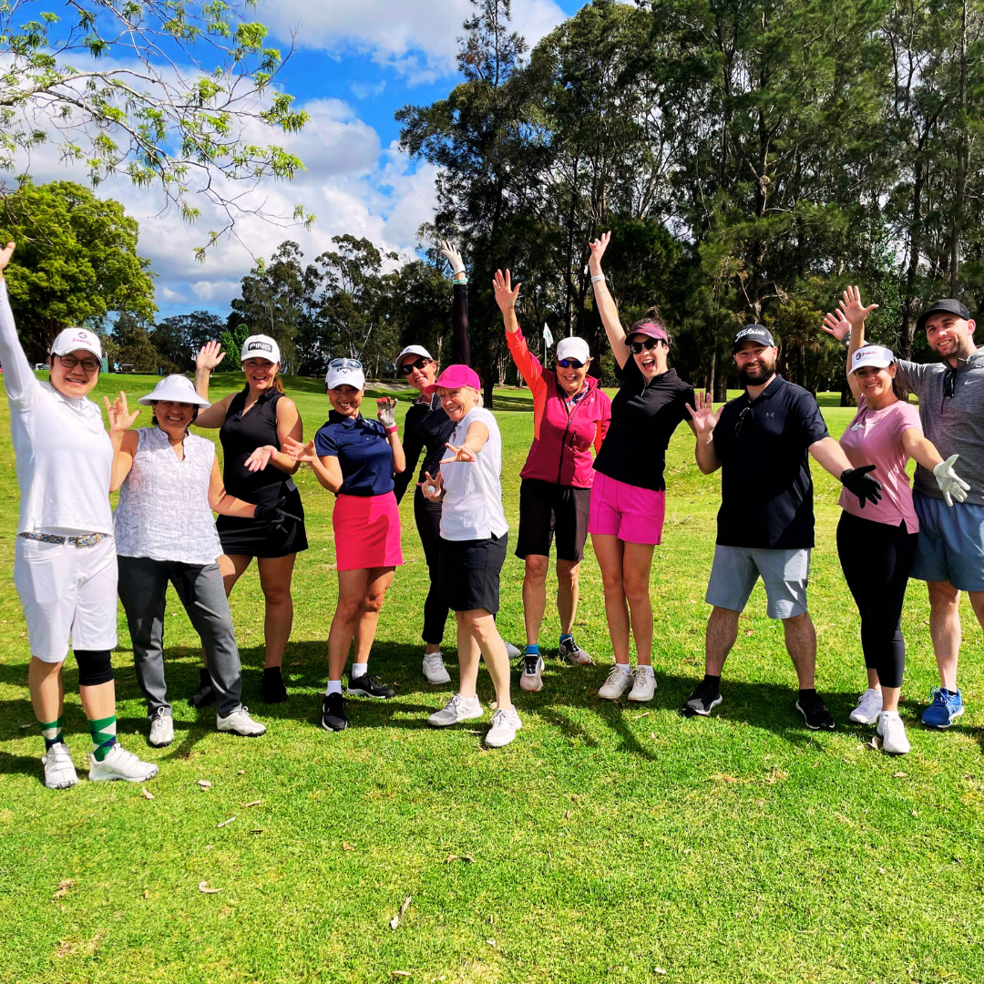 A group of golfers pose together on a sunny course, smiling with arms raised in celebration.